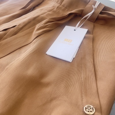 Calça bege clara com botão dourado e etiqueta branca pendurada