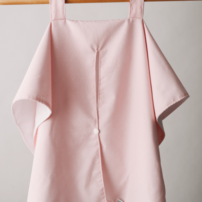 Pano de cozinha rosa claro com pontos pequenos e botão central pendurado numa barra de madeira