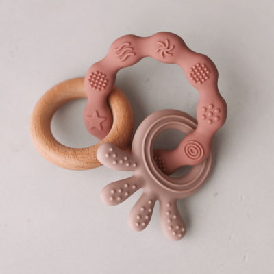 Dois brinquedos para bebés, um anel de madeira e um anel de silicone rosa texturizado