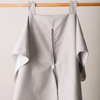 Capa cinzenta com pequenos pontos brancos pendurada num tubo de madeira.