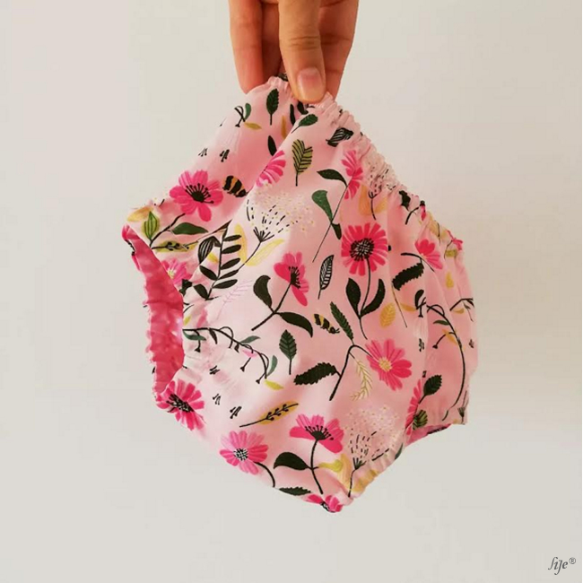 Cueca para bebé com padrão floral colorido segurada por uma mão