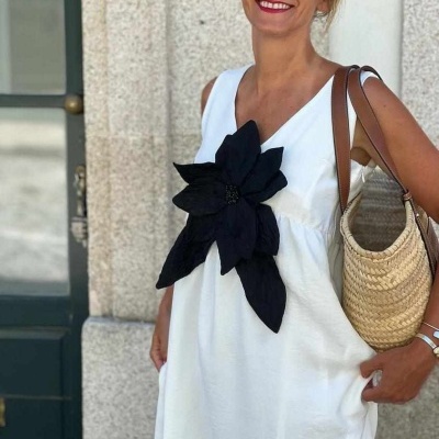 Vestido branco com grande flor preta no peito usado por mulher com mala de palha