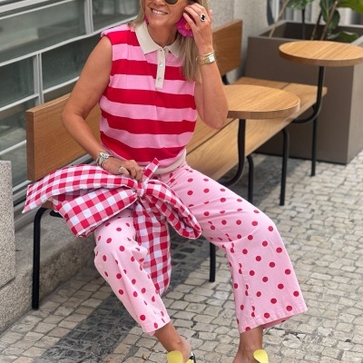 Mulher com roupa colorida sentada em banco de madeira ao ar livre, calçada portuguesa em fundo