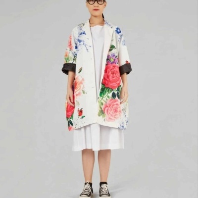 Casaco branco com padrão floral colorido usado por mulher com vestido branco e ténis pretos e brancos