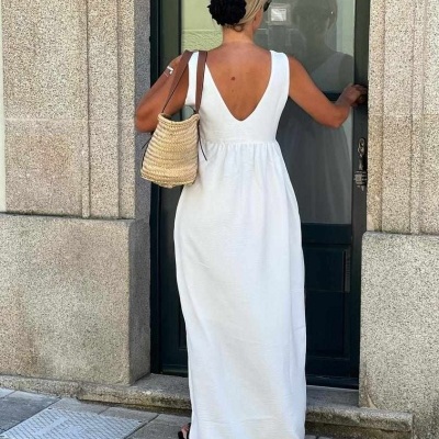 Mulher de costas a usar vestido longo branco com decote em V e mala de palha numa rua urbana