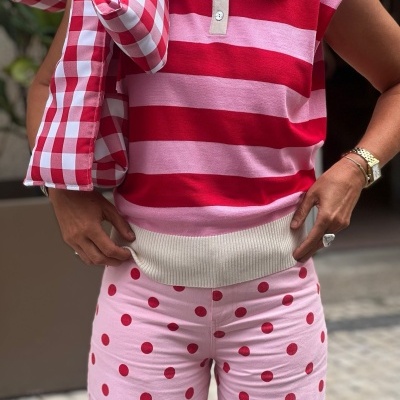 Conjunto com camisola riscada vermelha e rosa, calças rosa com bolinhas vermelhas e casaco xadrez dobrado no ombro