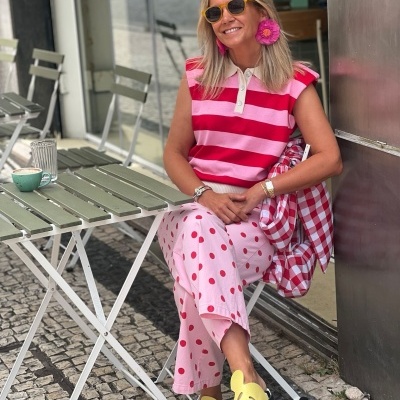 Mulher sentada numa cadeira ao ar livre com roupa colorida e sandálias amarelas