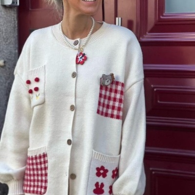 Casaquinho branco de malha com bolsos xadrez e detalhes vermelhos sobre fundo de porta vermelha.