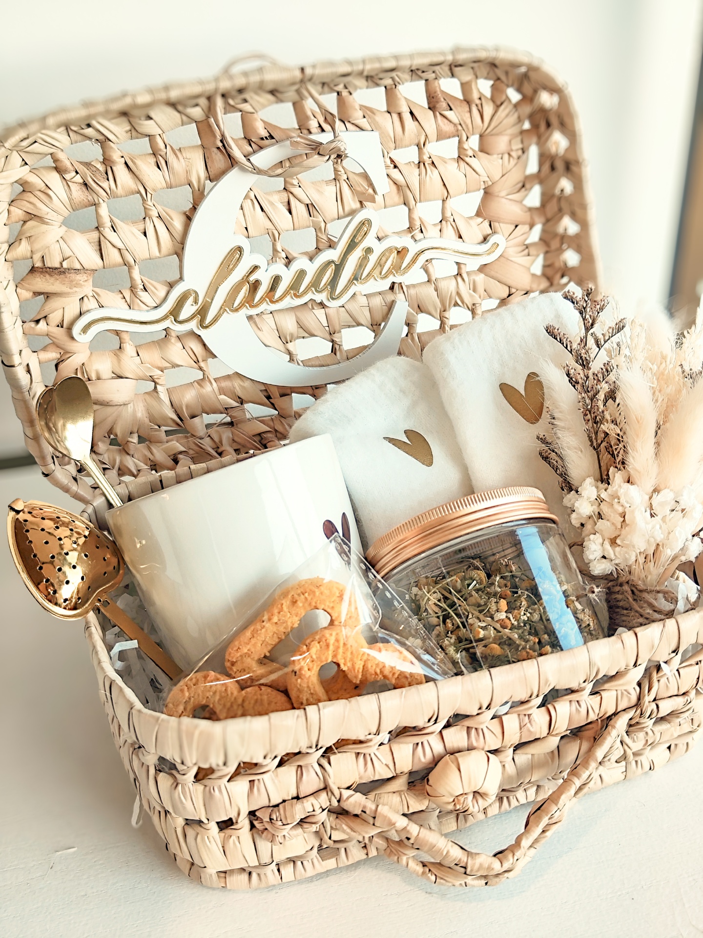 Cesto artesanal com chá, bolachas, colher e caneca, decorado com flores secas e logótipo Cláudia