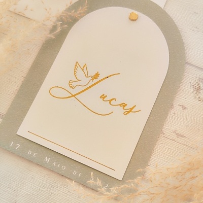 Convite ou cartão com nome Lucas, pomba e data numa superfície de madeira com ramos secos