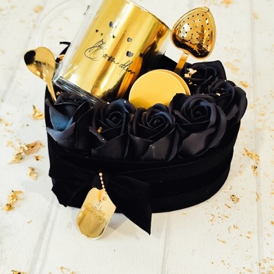 Conjunto de chá dourado com caneca, colher e infusor em caixa preta com rosas negras.