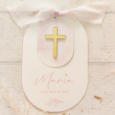 Etiqueta decorativa com cruz dourada e fita rosa claro em fundo de madeira clara