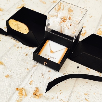 Colar com coração dourado em caixa preta com rosas brancas e papel dourado no fundo branco