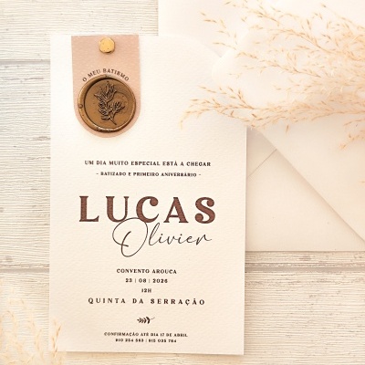 Convite creme com selo dourado para batismo e aniversário ao lado de envelope e flores secas
