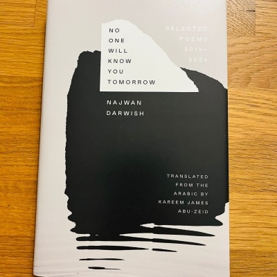 Livro No One Will Know You Tomorrow de Najwan Darwish com capa branca e preta sobre madeira.