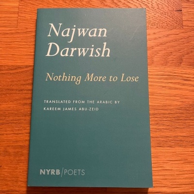 Livro Najwan Darwish Nothing More to Lose com capa verde-azulada em cima de mesa de madeira