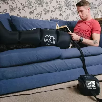 Homem sentado no sofá azul com bota de compressão preta AIR RELAX.