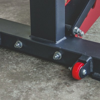 Base de estrutura metálica preta com parafusos e roda vermelha sobre chão de cimento