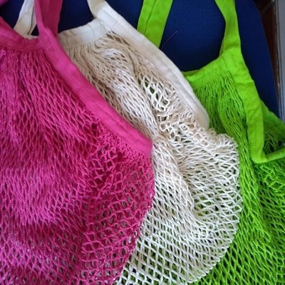 Sacos de rede coloridos em tecido rosa, branco e verde sobre fundo azul