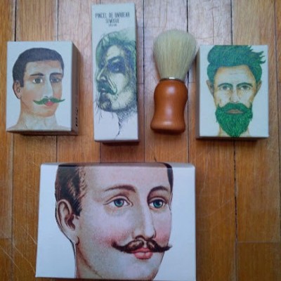 Produtos para barbear com ilustrações de homens e uma escova de barba sobre chão de madeira