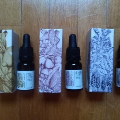 Três frascos de vidro escuro com conta-gotas e respetivas caixas com desenhos botânicos em chão de madeira.