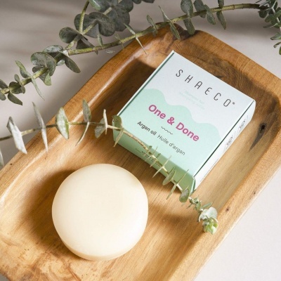 Sabonete redondo bege claro com embalagem branca e verde em prato de madeira, decorado com raminhos de eucalipto
