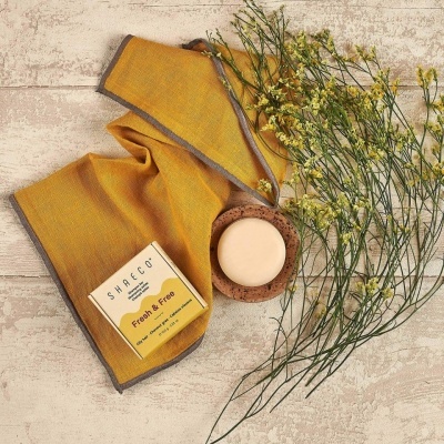 Conjunto de cuidados pessoais com toalha mostarda, sabão redondo e flores amarelas