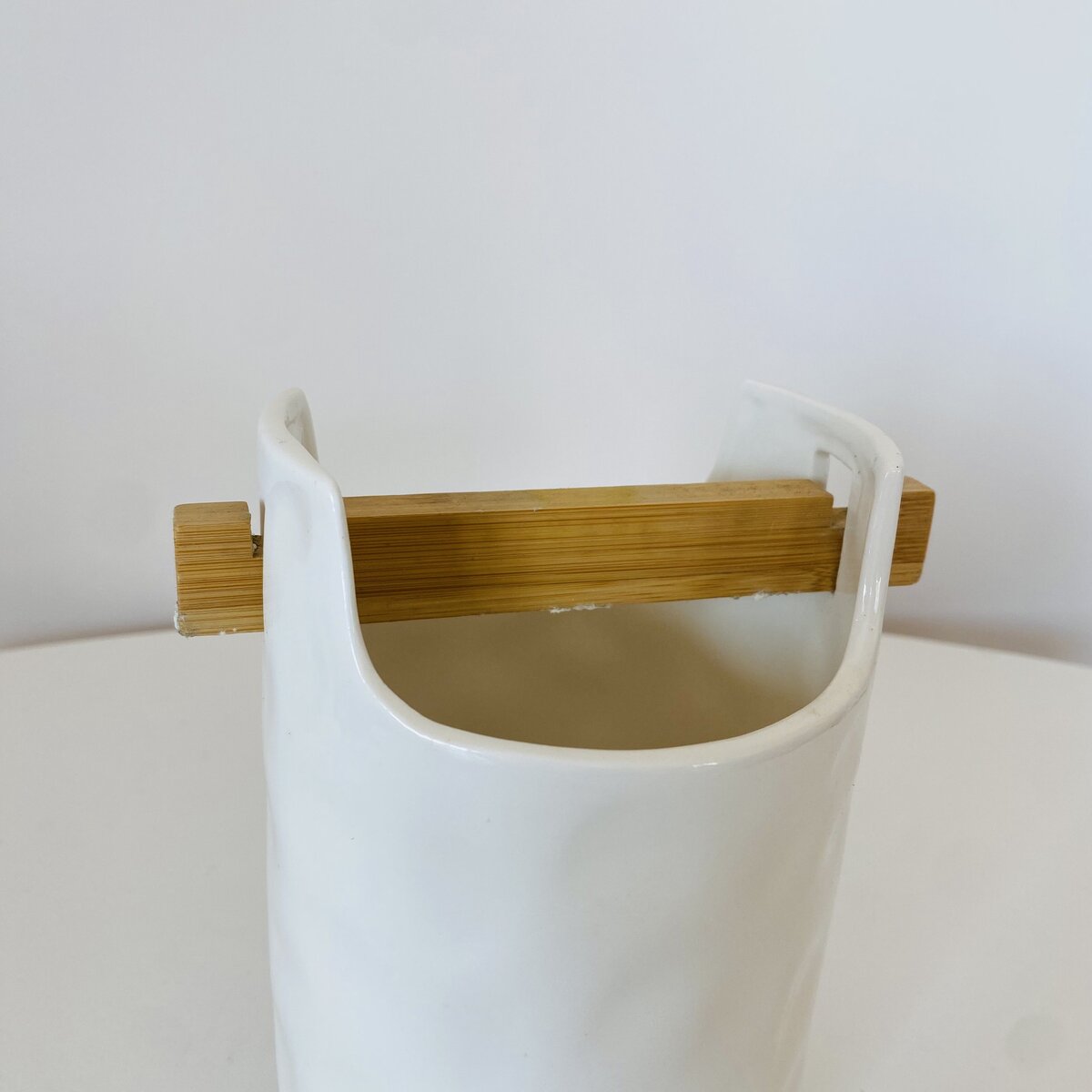 Vaso branco de cerâmica com suporte de madeira clara