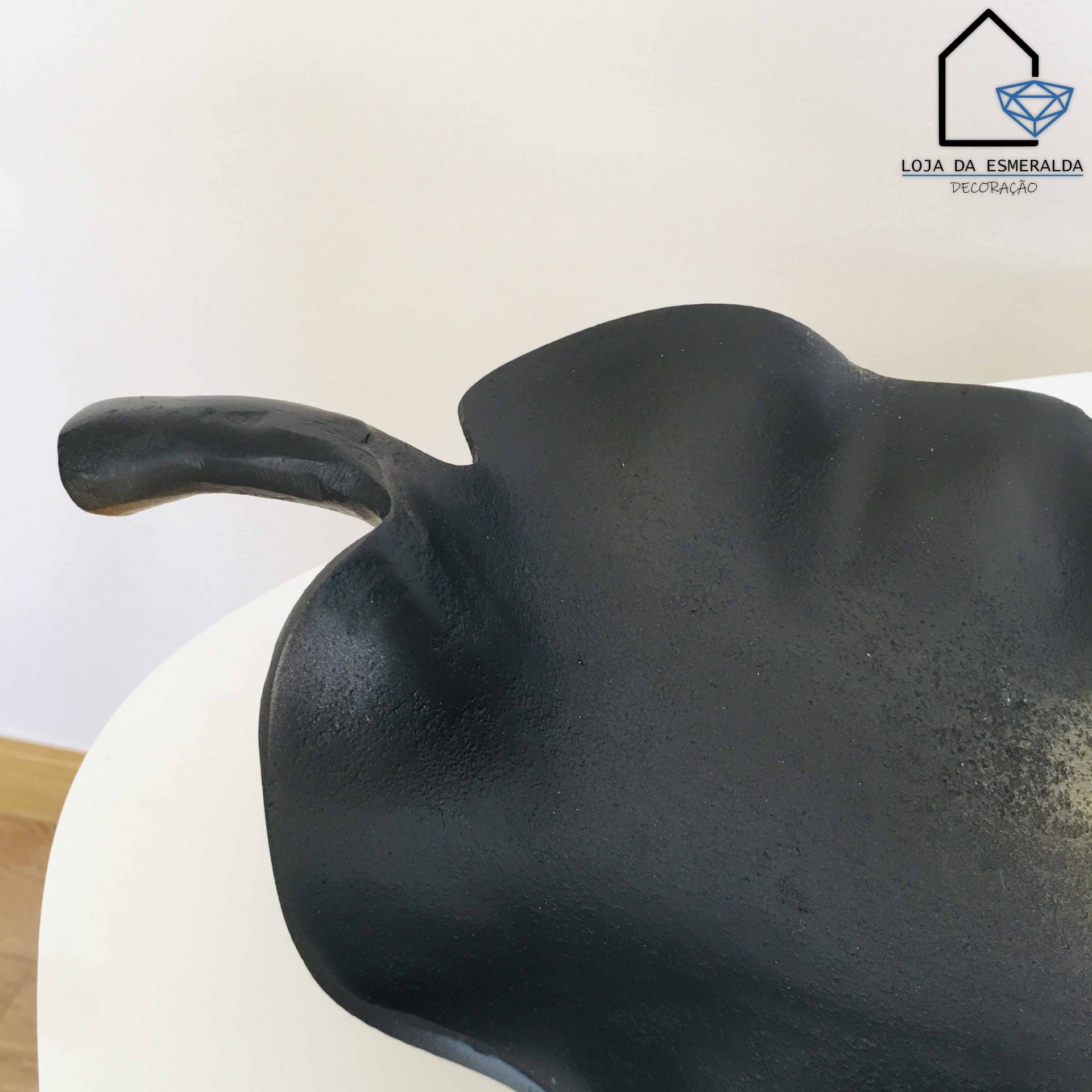 Escultura metálica preta decorativa com textura irregular em mesa branca