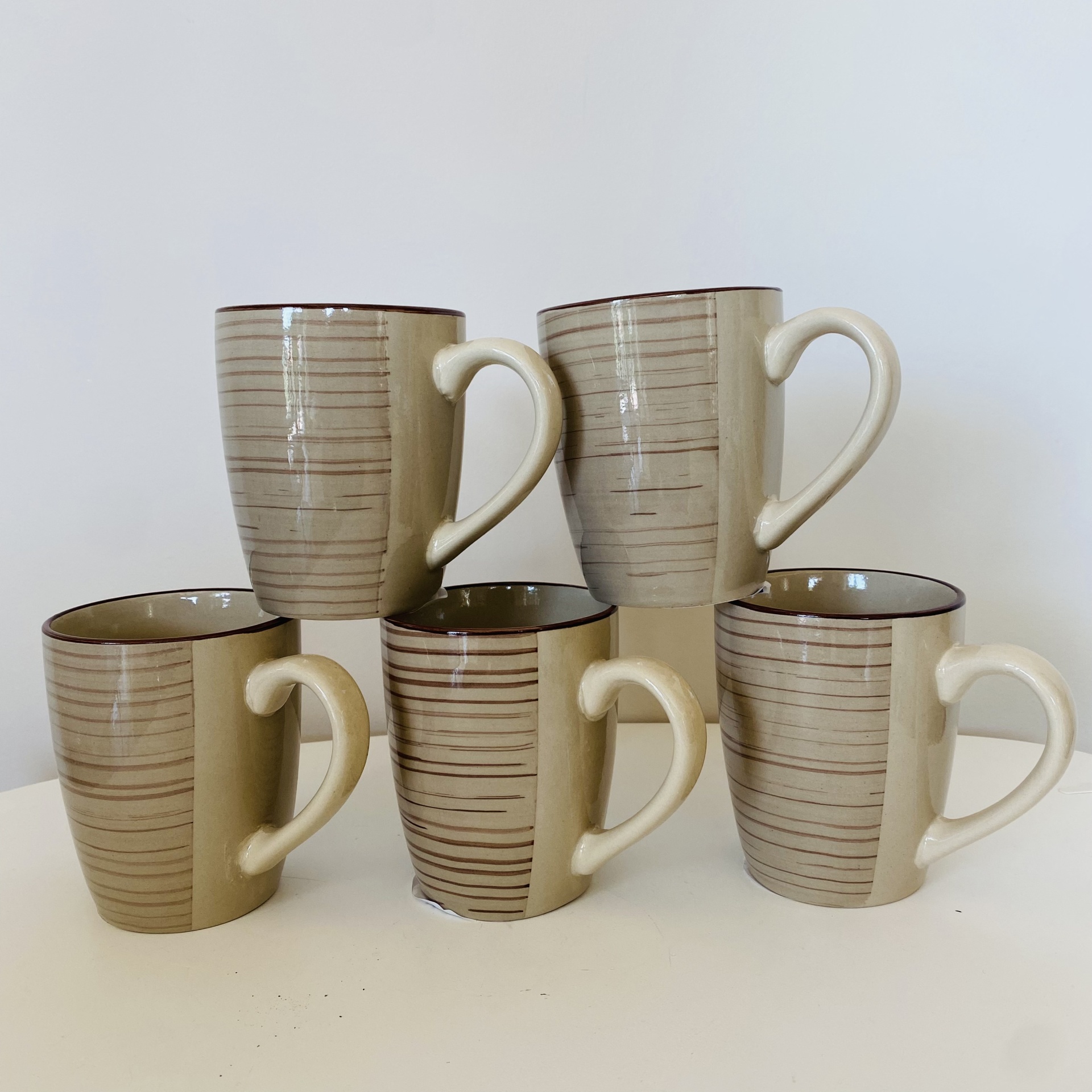 Cinco canecas de cerâmica bege com riscas horizontais pretas e interior castanho