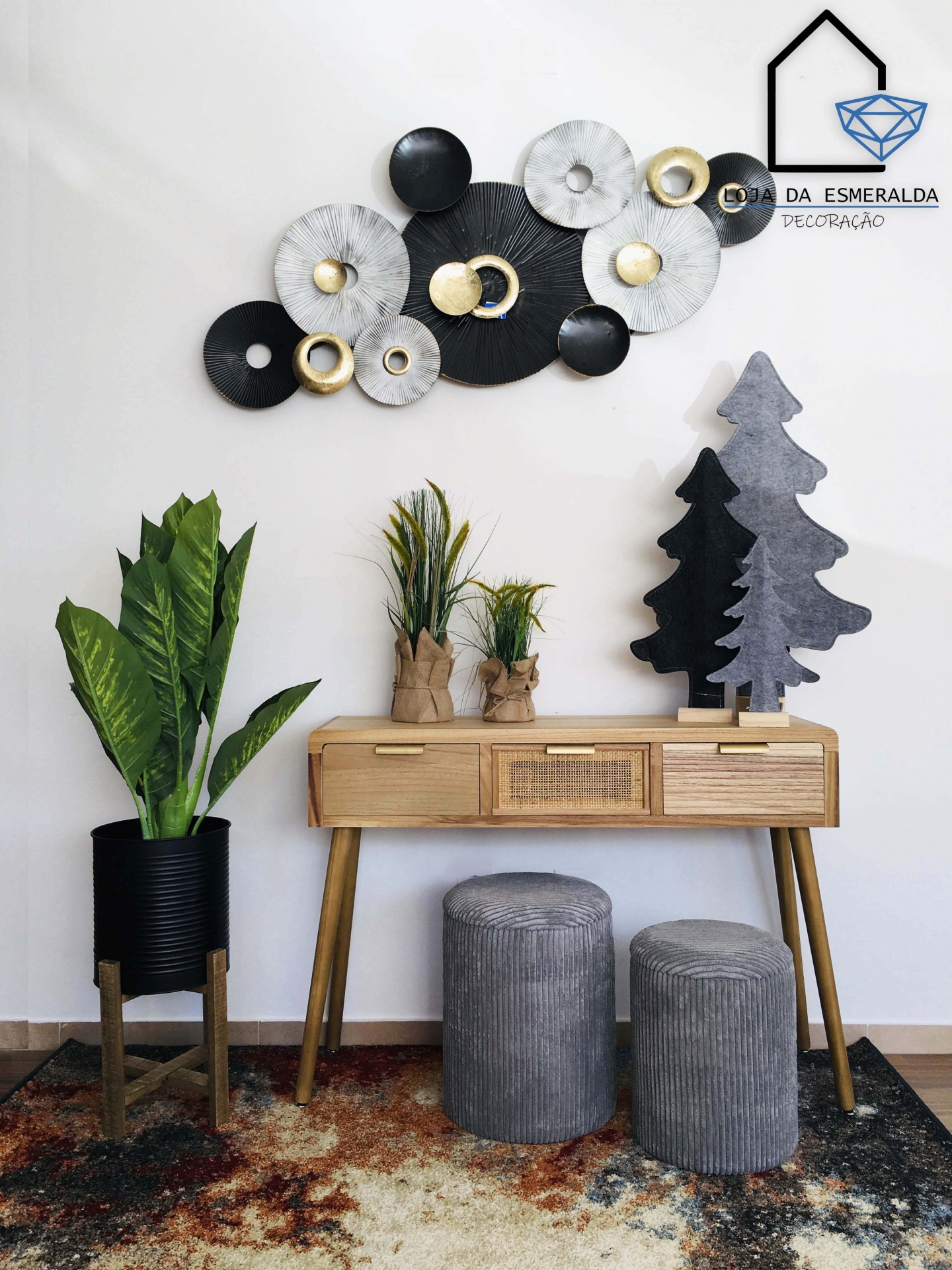 Decoração de parede em círculos metálicos cinza, preto e dourado acima de móvel de madeira com plantas e pufes em sala decorada
