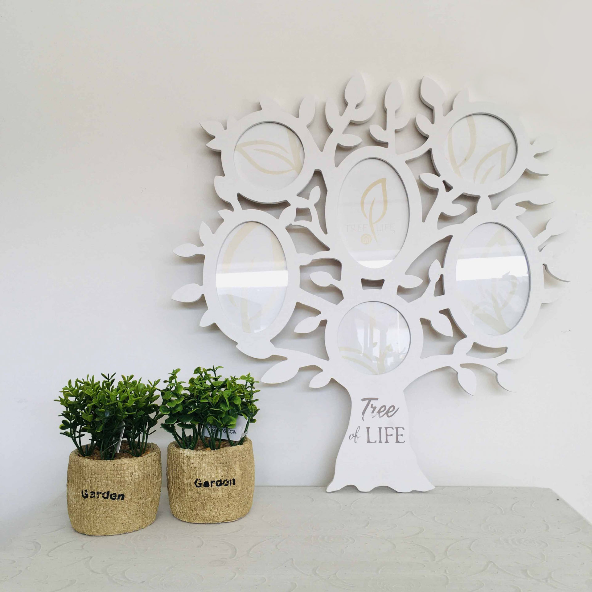 Árvore decorativa branca com molduras para fotos e duas plantas em vasos de tecido