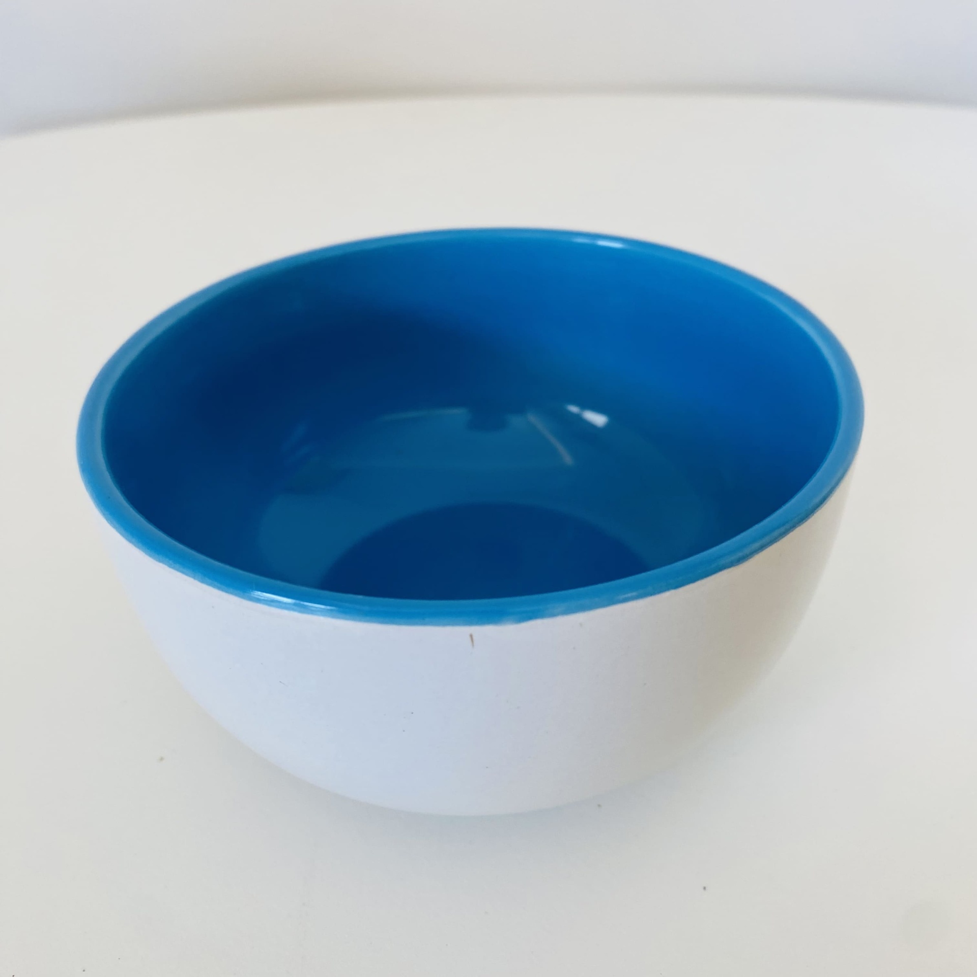 Taça pequena com interior azul e exterior branco sobre fundo branco