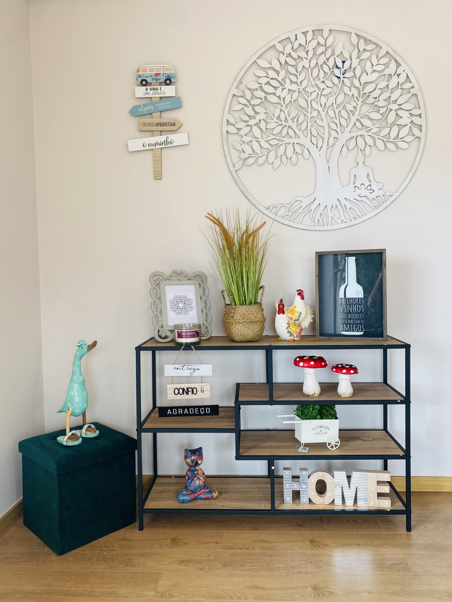 Estante decorativa com objetos e decoração na parede, incluindo escultura de árvore e placa com texto em português.