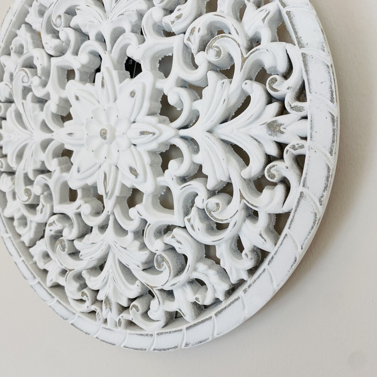 Elemento decorativo circular em madeira branca com padrão floral e arabescos