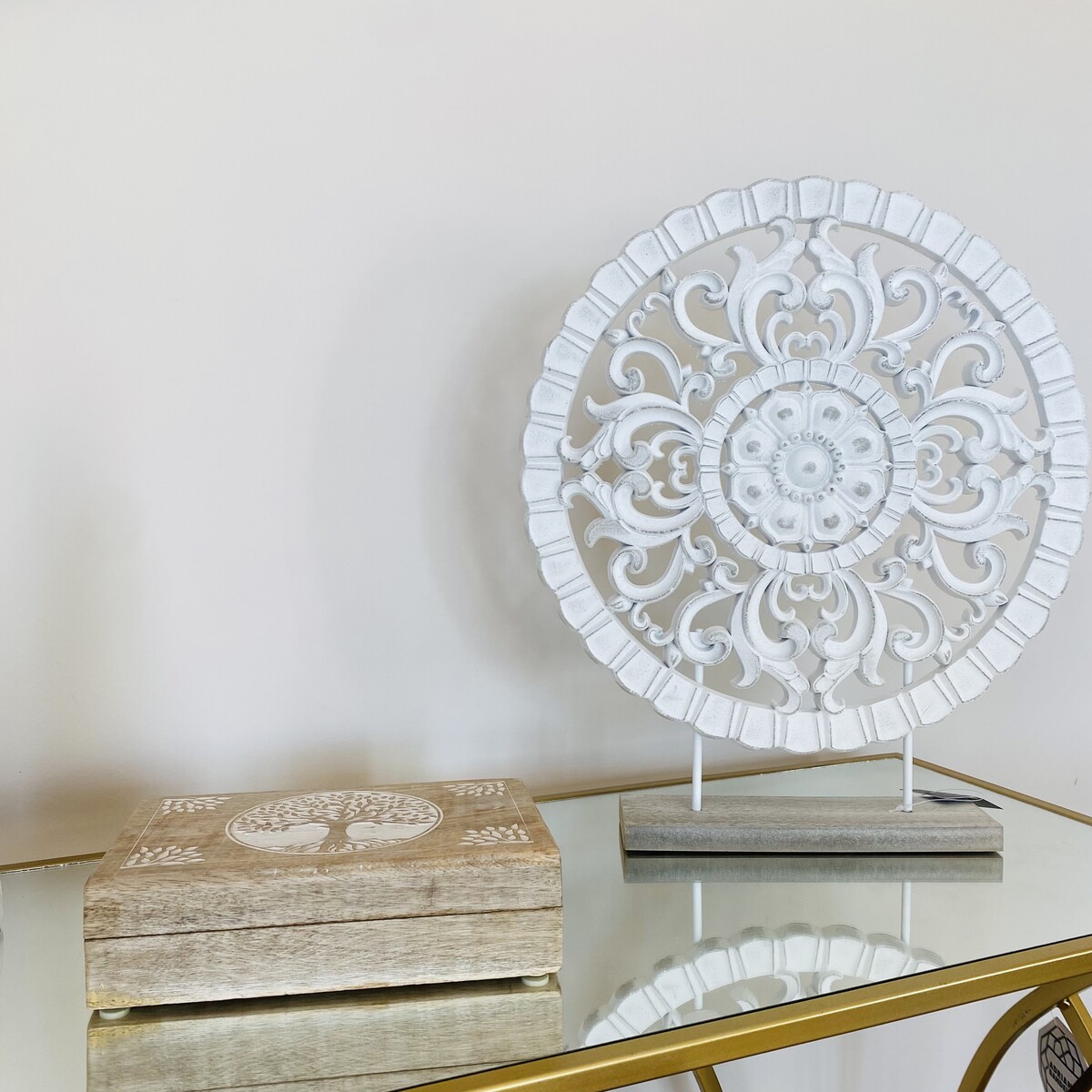 Mandala decorativa branca em suporte com caixa de madeira clara numa mesa de vidro dourada