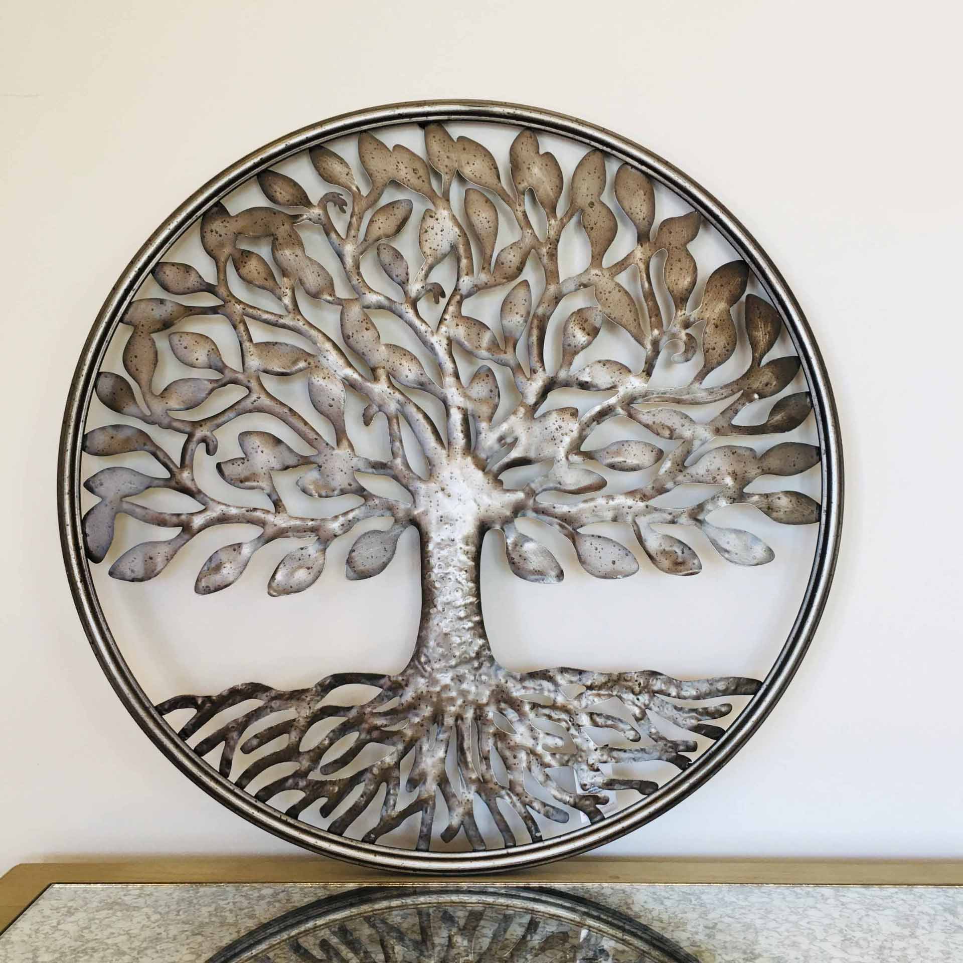Escultura metálica circular de árvore com folhas e raízes na parede