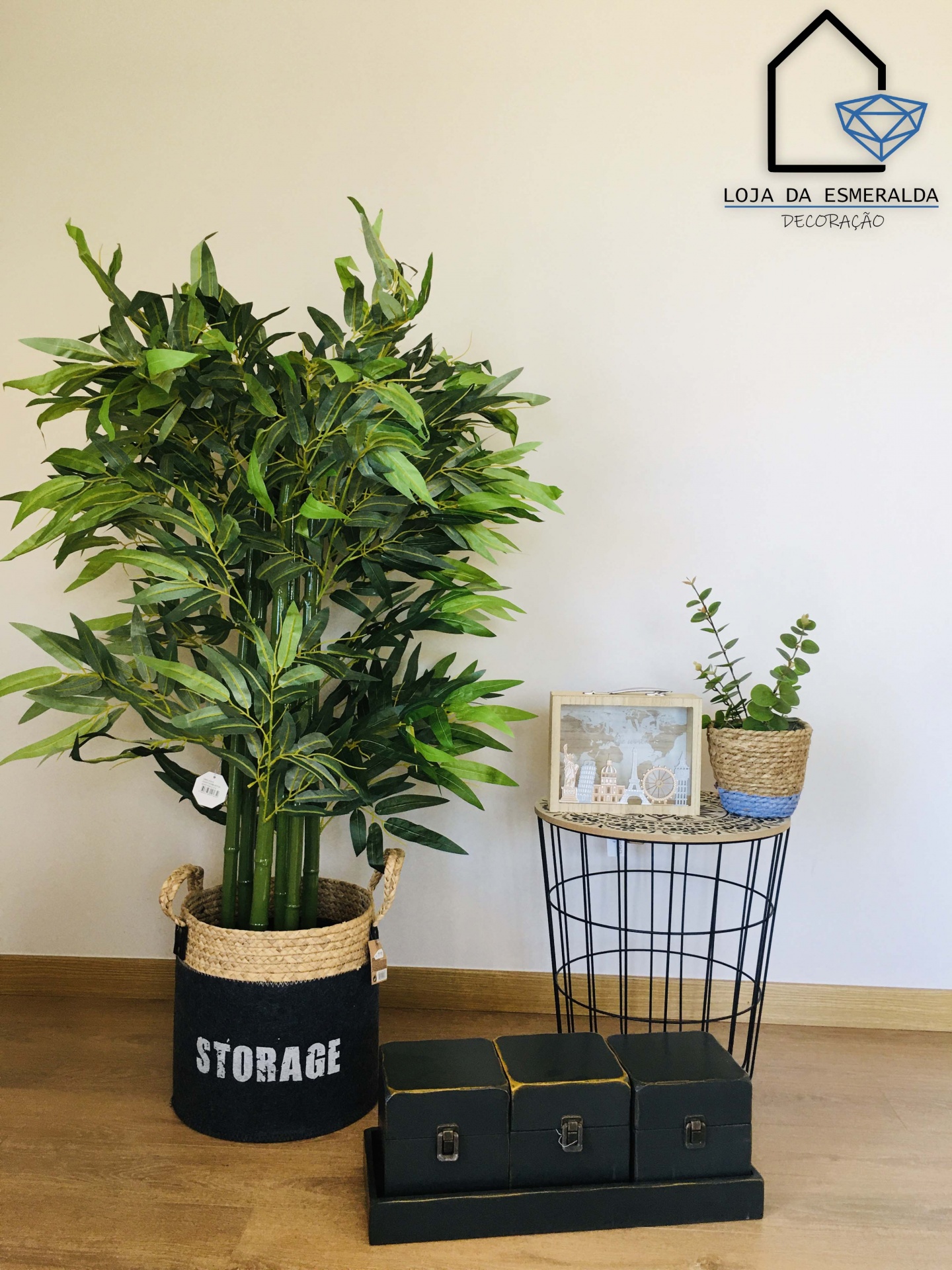 Planta artificial em vaso preto com STORAGE, mesa de metal com vasos e caixas pretas organizadas no chão