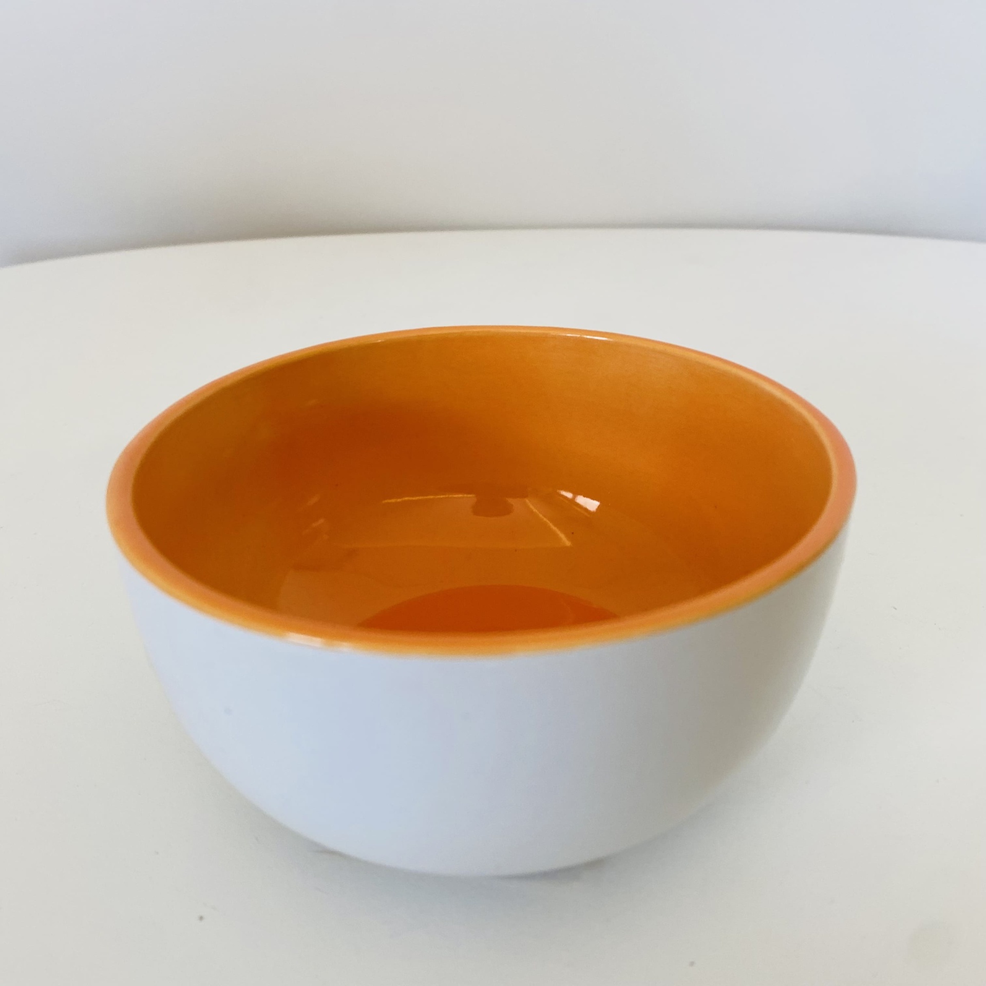 Tigela de cerâmica branca por fora e laranja por dentro numa superfície branca