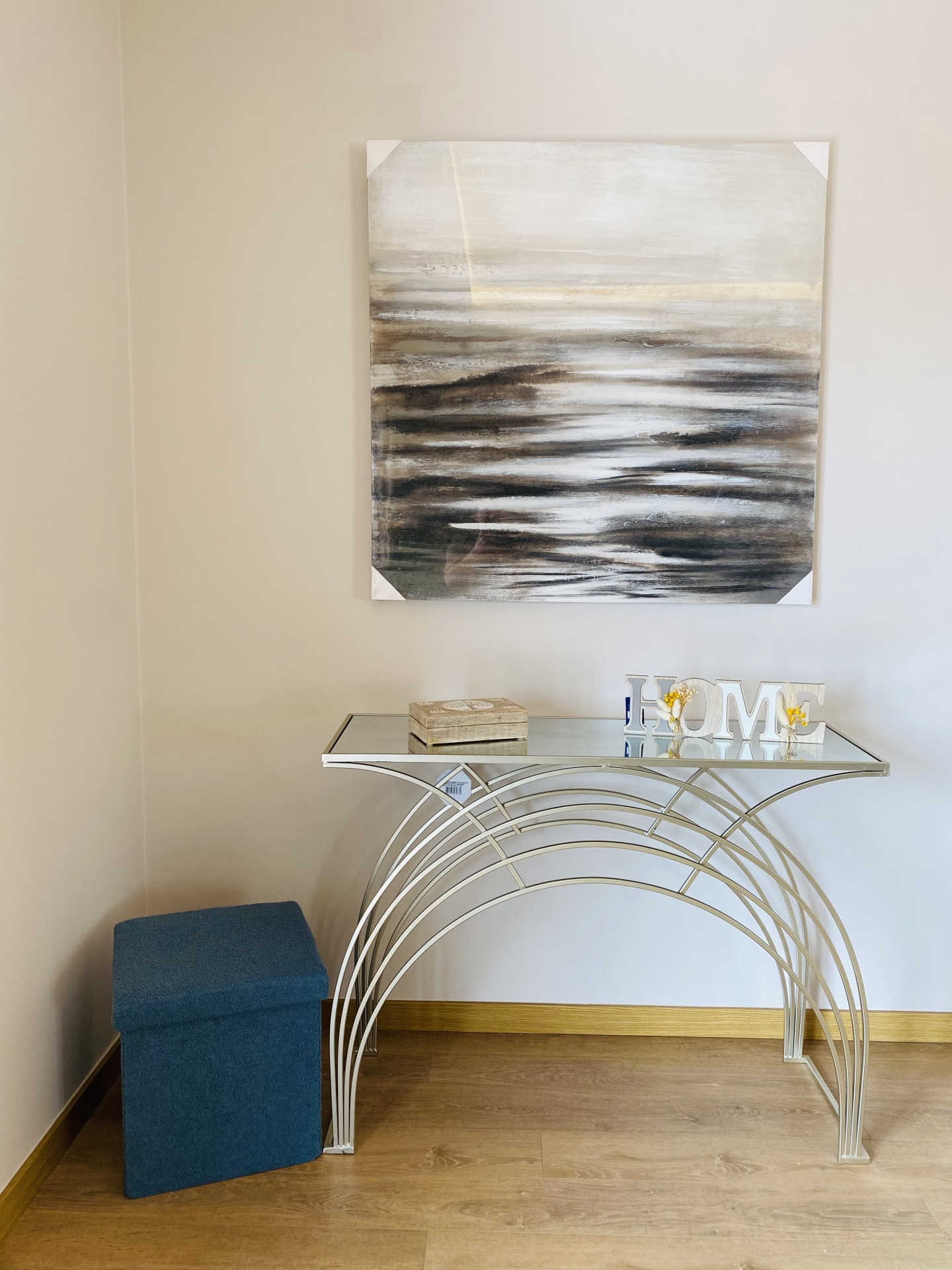 Mesa de vidro e metal com pintura abstrata e puff azul num canto de parede