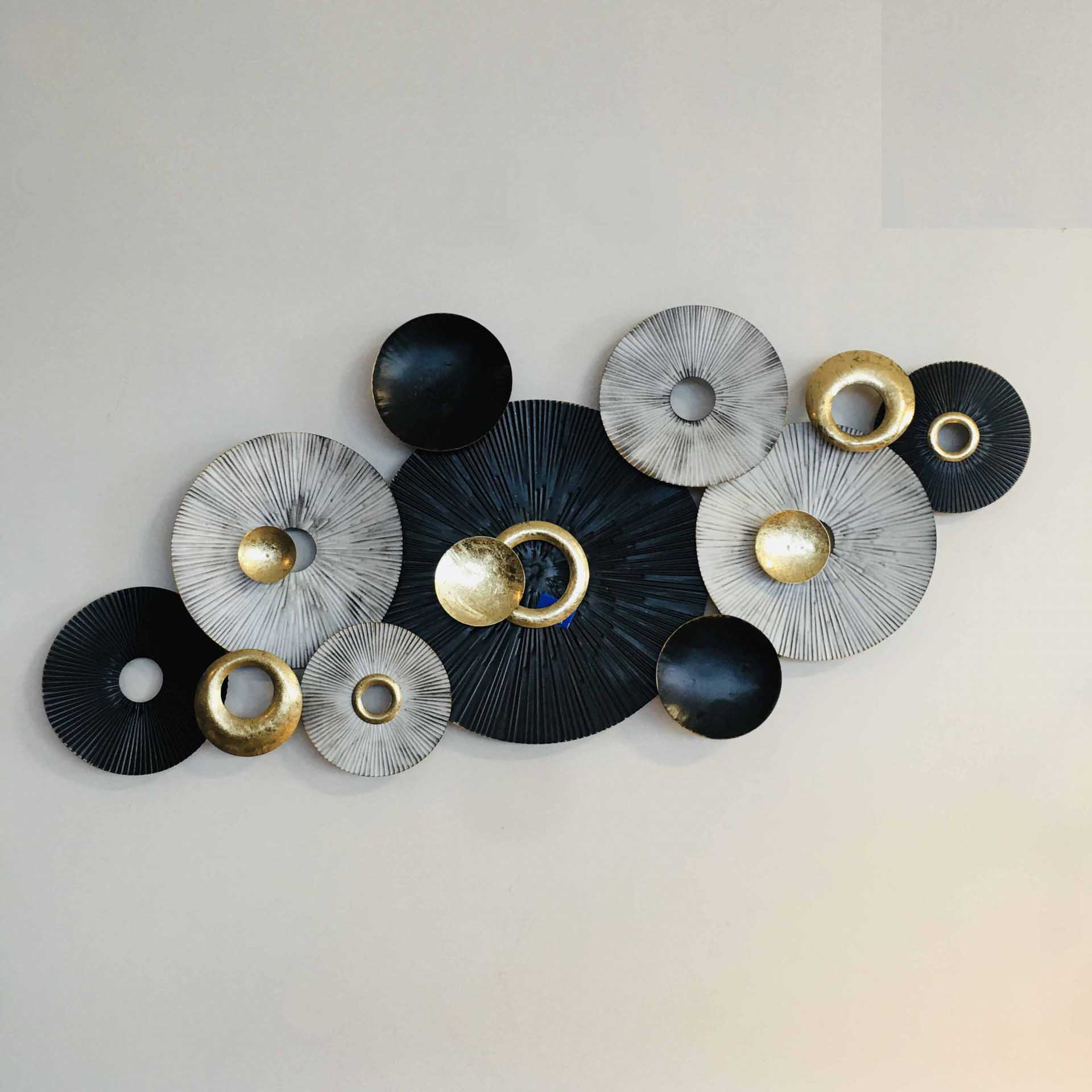 Decoração de parede com círculos metálicos em preto, branco e dourado em textura e relevo.