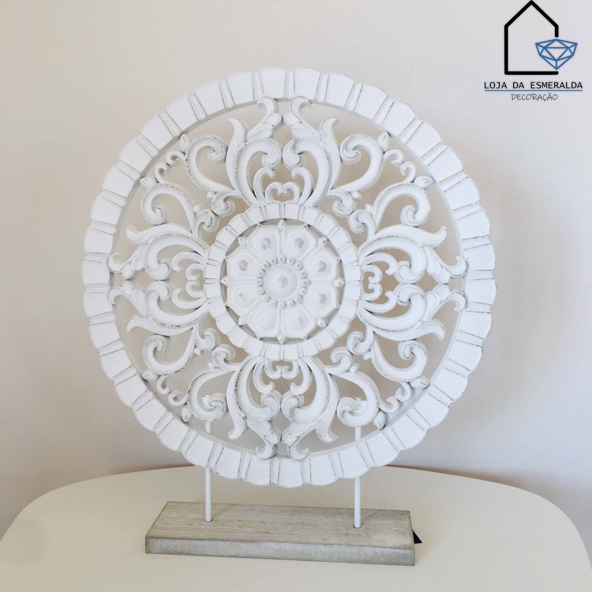 Ornamento decorativo redondo branco com padrões florais em madeira sobre mesa branca