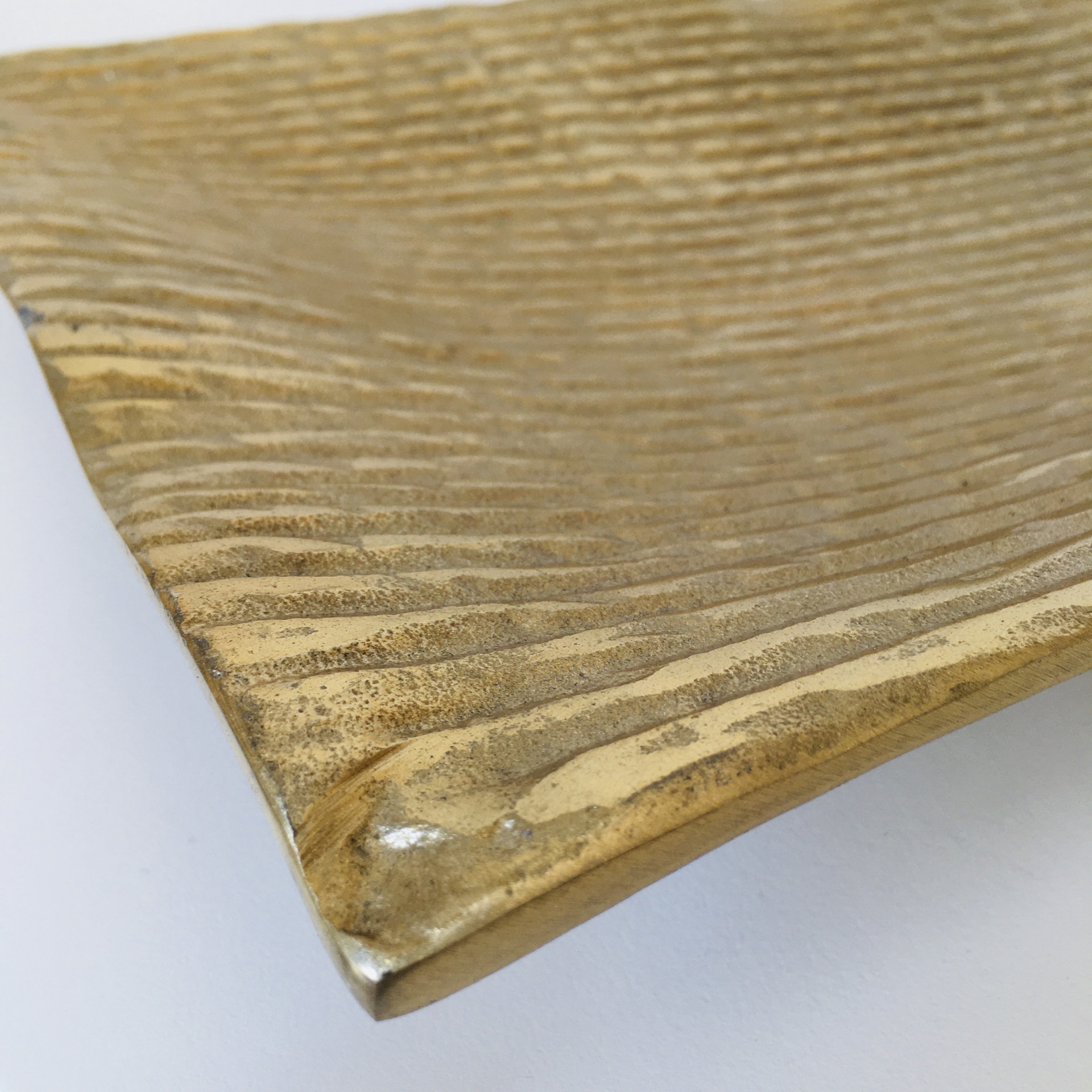 Placa decorativa metálica dourada com padrão ondulado em relevo