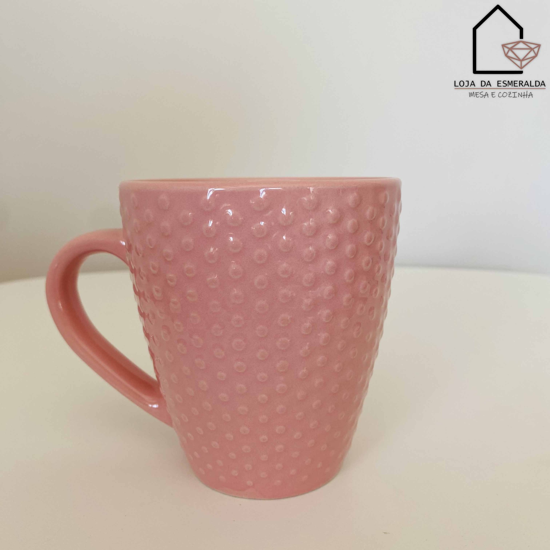 Caneca rosa com textura de bolinhas e asa grande sobre mesa branca