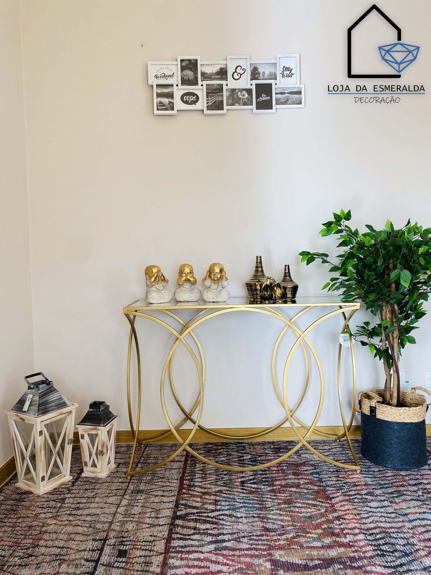 Consola dourada com decoração, lanternas, planta e quadro na parede branca.