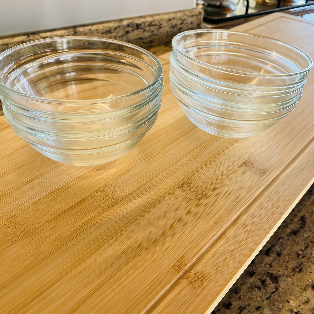 Dois conjuntos de taças de vidro transparentes sobre tábua de madeira clara