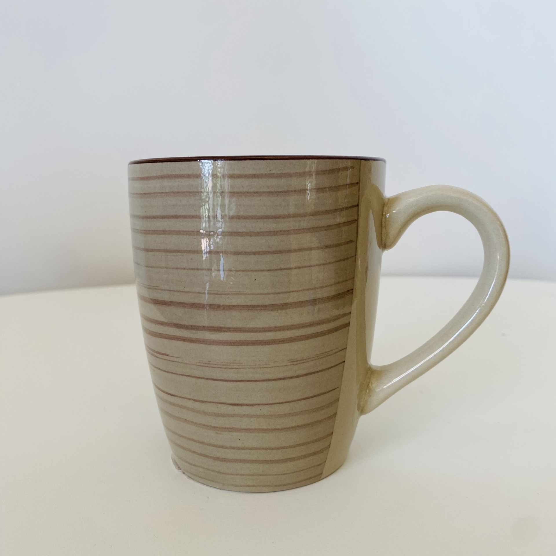 Caneca de cerâmica bege com riscas horizontais marrons