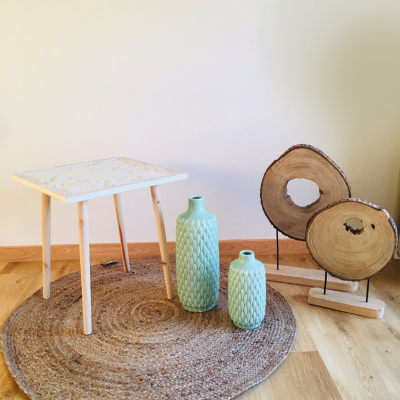 Mesa branca com vasos cerâmicos verdes e decoração de madeira sobre tapete redondo