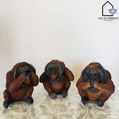 Três estatuetas de macacos em resina castanha em diferentes poses sobre superfície branca decorativa
