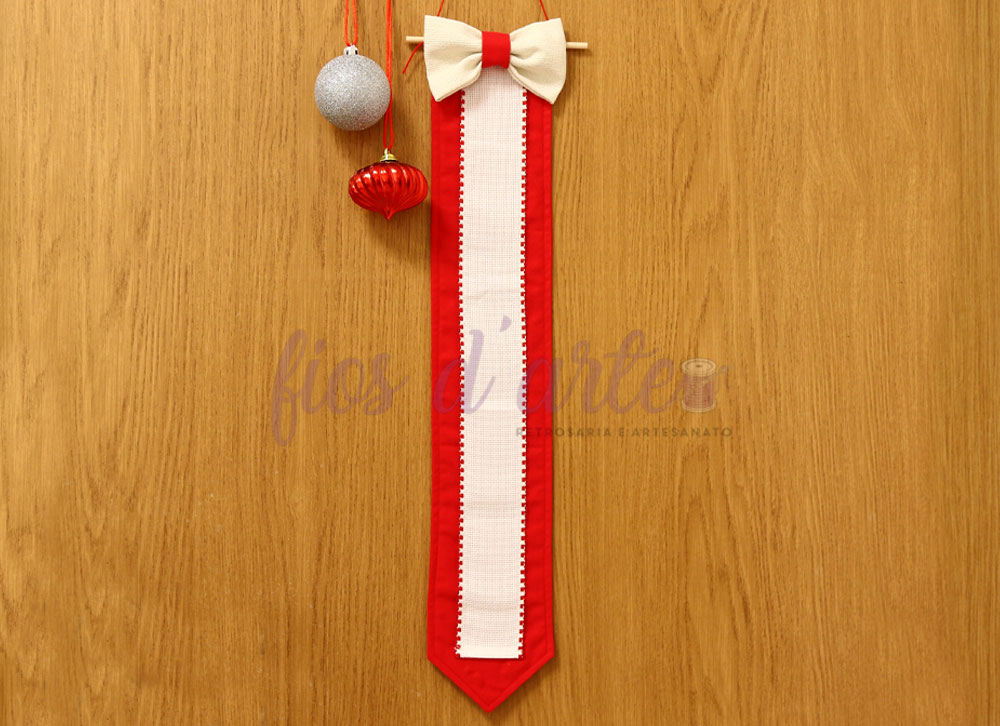 Gravata decorativa de feltro com laço pendurada numa parede de madeira com bolas de Natal